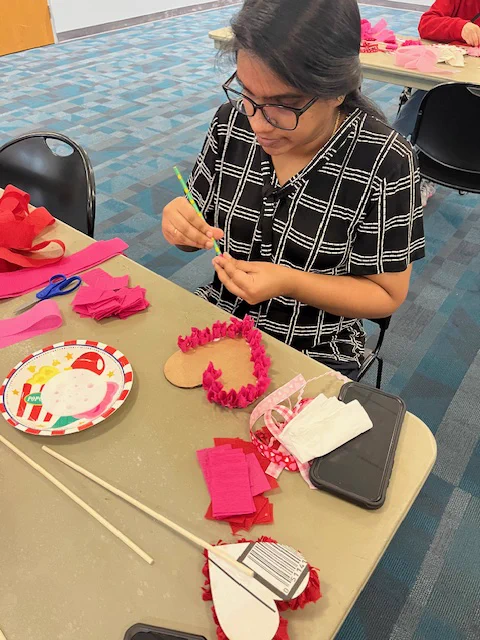 A library patron rolls up crepe paper florets to glue on a heart-shaped cardboard backing. 