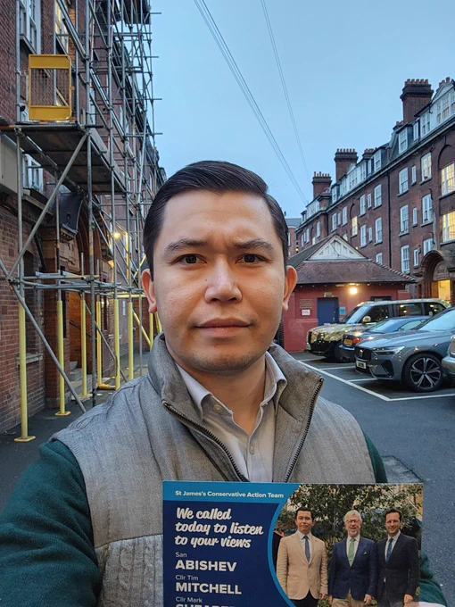 Man holding a political leaflet, with red brick bulding facades in the background. 