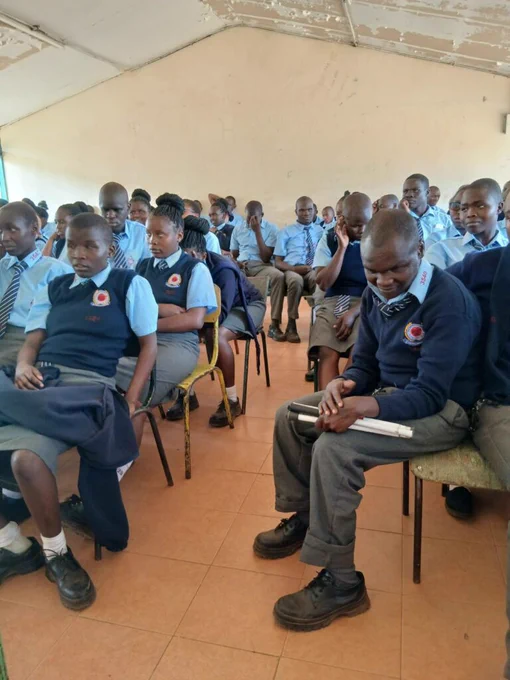 Students in school uniforms seated in a classroom attentively listening to a lesson or presentation.
