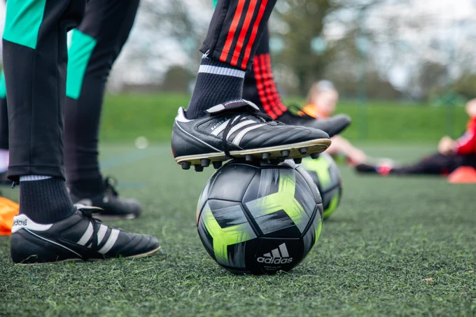 A close-up shot of a coach's foot showing their football boot controlling a football.