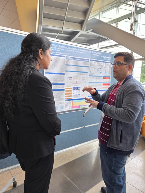 Two individuals engaged in a discussion in front of a scientific poster at a conference.