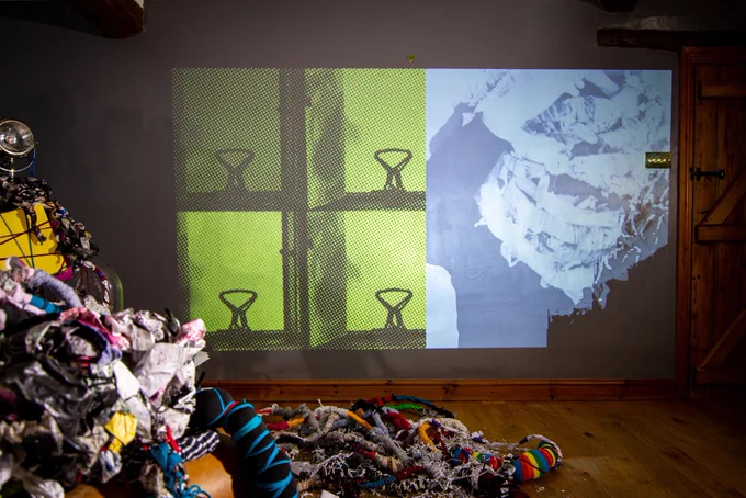 The chair of forms face a film projected on the wall of box files and forms twisted around a persons head