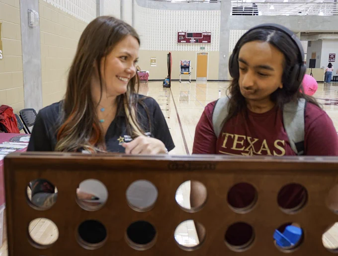 A staff member from the Information Security Office and a Texas State student interact with each other behind a Connect 4 board game. 