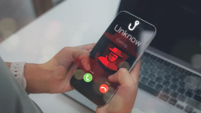 Person holding a smartphone displaying an incoming call from an unknown number with a hacker icon.