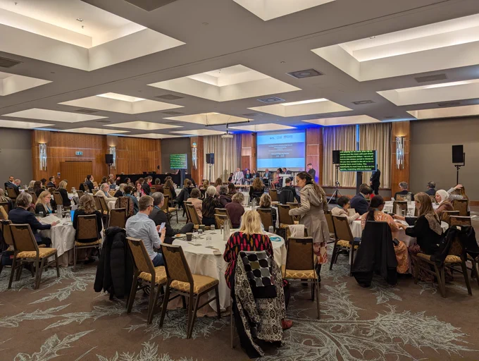 A group of people sit in a large conference room facing towards a stage and large screen at the GLAD AGM in Edinburgh