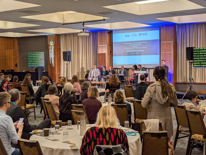 A group of people sit facing a stage of mixed panellists as they sit in front of a large screen during the GLAD AGM 