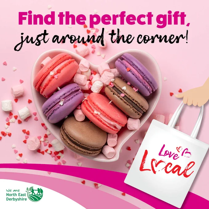 Heart-shaped bowl with pink, purple, and brown macarons surrounded by marshmallows. Text: "Find the perfect gift, just around the corner!" with a "Love Local" tote bag. North East Derbyshire logo at the bottom.