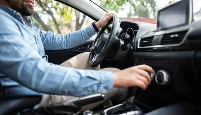 Driver adjusting the air conditioning controls inside a car for heat control