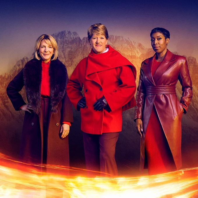 Three women in red coats stand against a backdrop of a snowy mountain with a streak of fire across the foreground