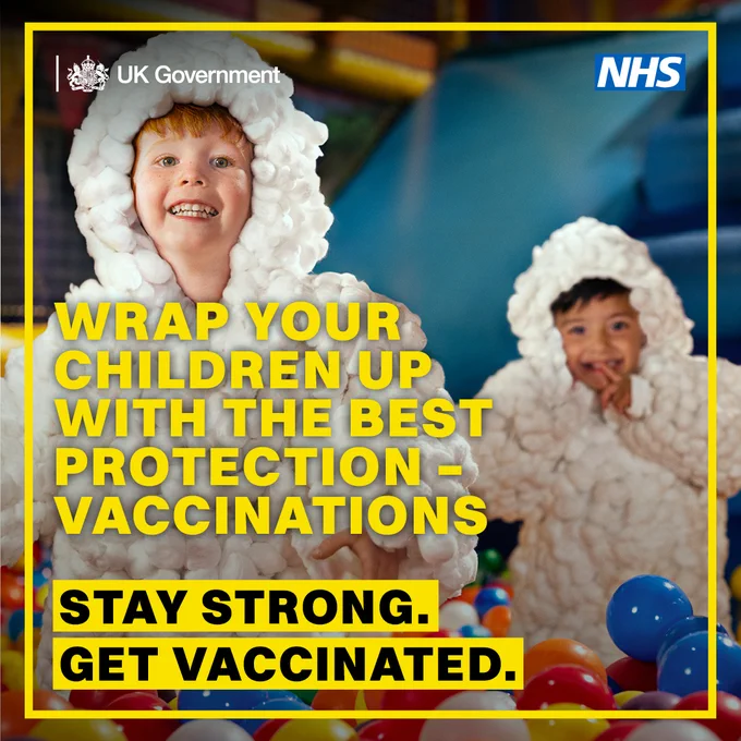 Two children wearing fluffy white cottonwool outfits sit in a colourful ball pit. Bold yellow text reads: “Wrap your children up with the best protection – vaccinations.” Below, a yellow box with black text says: “Stay strong. Get vaccinated.” Logos for the UK Government and NHS appear at the top.