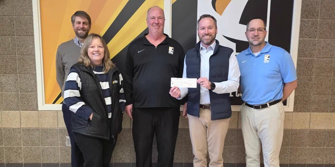 Five individuals standing in front of a yellow and black background at Anoka Technical College. One is holding a check. 