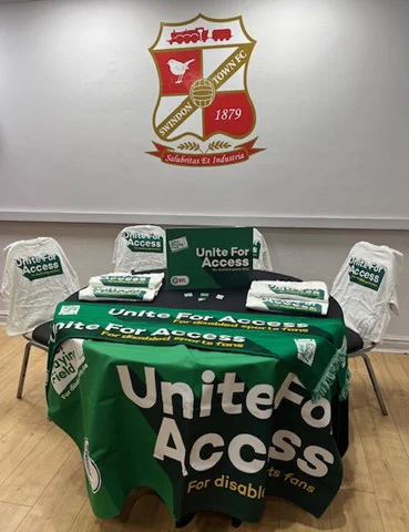 A table with with a green tablecloth and chairs.
