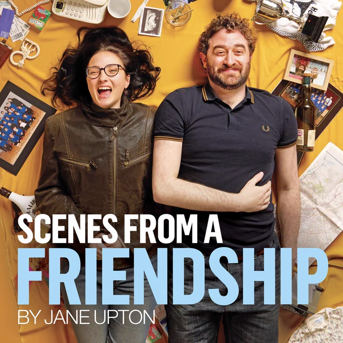 A man and a woman are lying on their backs, surrounded by the memorabilia of their lives – old photos, school trophies, babygros, cigarette butts, soft toys and empty bottles. They are both laughing hard. 