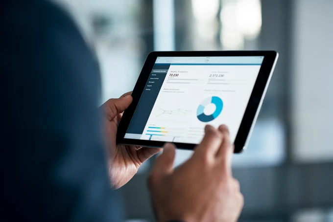 A person holding a tablet displaying financial graphs and data.