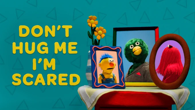 Key art for "Don't Hug Me I'm Scared" on Dropout shows its title along with its three principal puppet characters in picture frames.