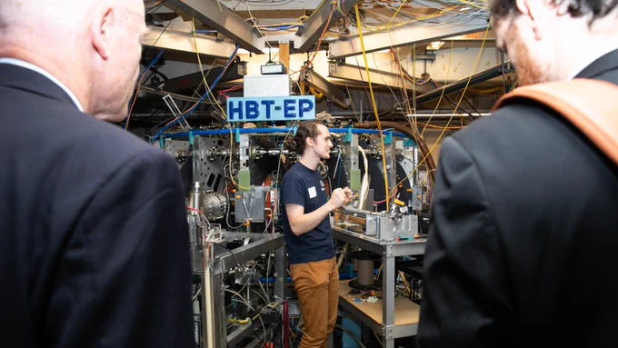 A student stands infant of a fusion experiment. Two men are looking on and listening.