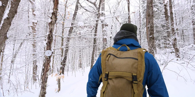 a park visitor in a blue coat hiking on a snowy trail with a brown backpack on facing away from the camera.