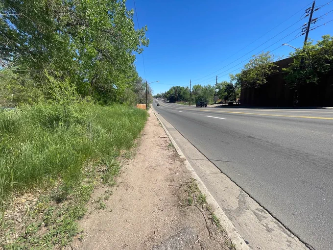 A vehicle travels along a section of Sheridan Boulevard in the Denver area. A wall of grass and trees are seen along the shoulder of the road.