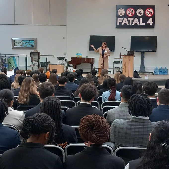A group of school pupils sitting in a school hall looking at a person presenting 