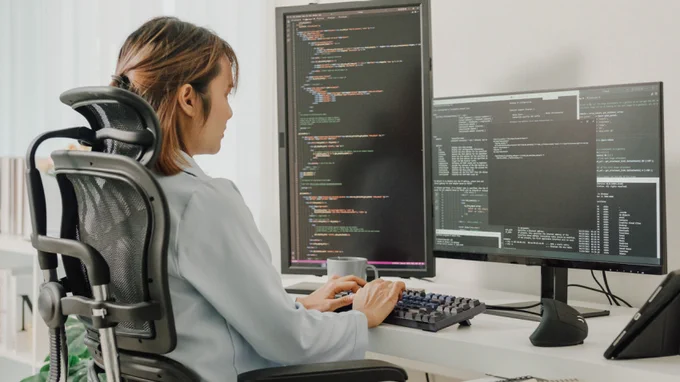 An image of person sitting at a desk with a computer screen, coding.