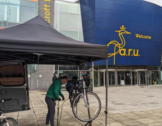 A mechanic working on a bike in front of a blue building.