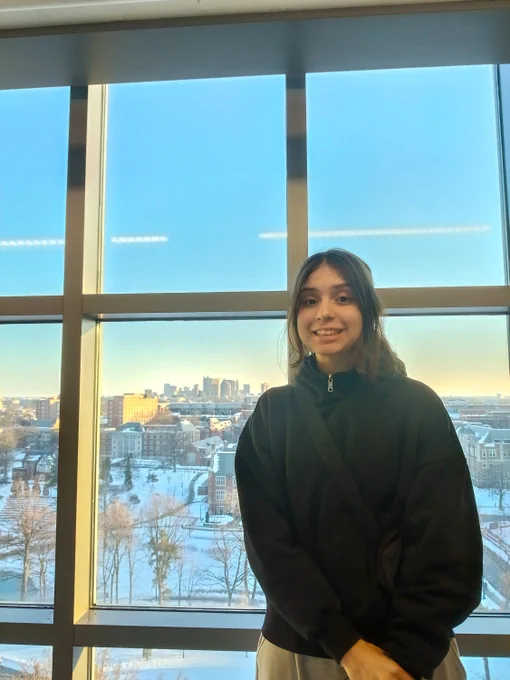 Woman standing inside in tall building with city in background.
