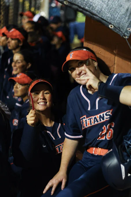 Two Fullerton players smiling. One has a peace sign against her face.