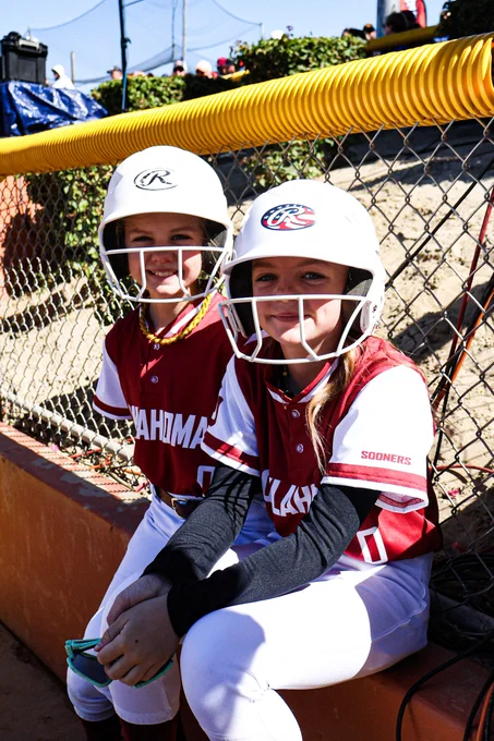 Two Oklahoma bat girls in white helmets smiling
