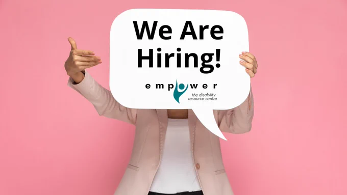 A person dressed in business casual holds a paper speech bubble in front of their face, pointing towards it with the right hand. On the speech bubble, text reads We Are Hiring with the Empower N L logo beneath.