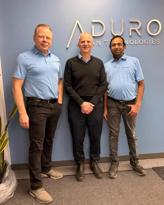 Abe Dyck, Don Fusco, and Anil Jhawar pose in front of the Aduro Clean Technologies logo at Aduro's London site.
