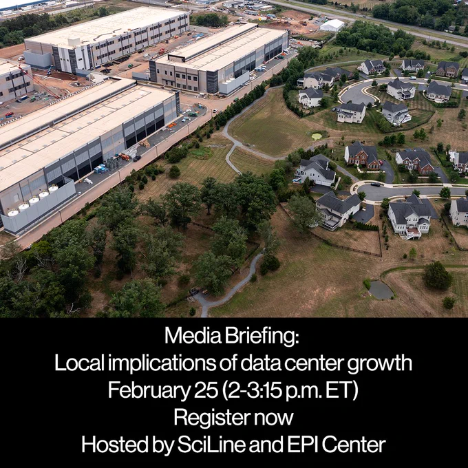 Aerial view of a large data center complex adjacent to a suburban neighborhood with houses and green spaces.