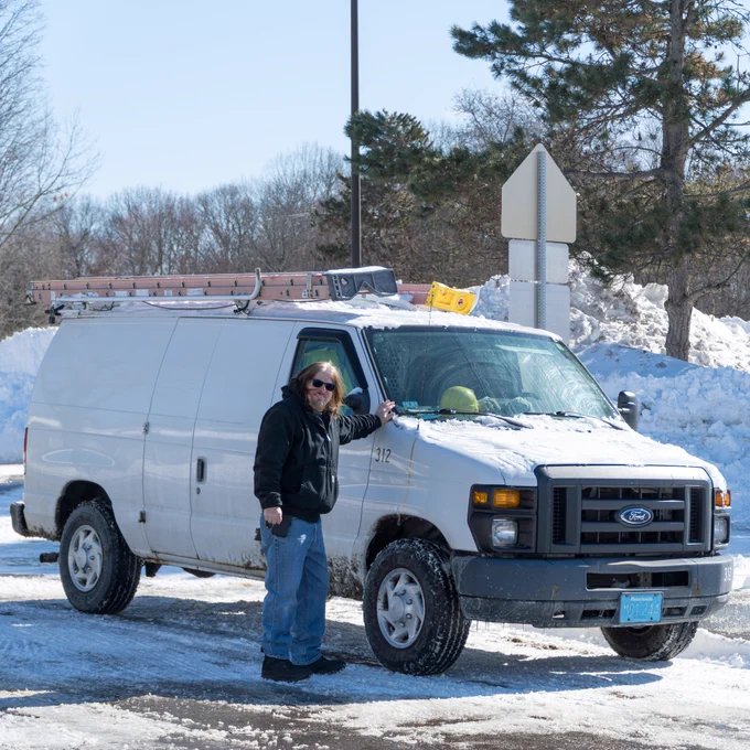 An MPS facilities member stands next to a white van outside a snow-covered parking lot.