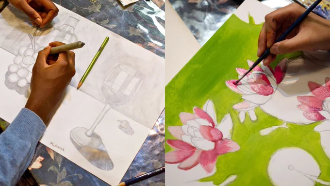 Two hands are visible in the image, each working on a separate piece of art. On the left, a pencil drawing depicts a glass, grapes, and a bottle. On the right, a brush is being used to paint pink flowers over a green background.