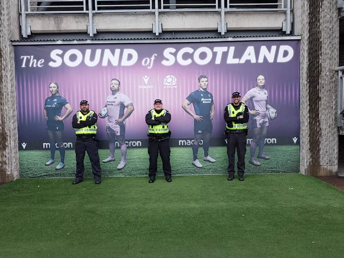 Three Project Servator police officers standing in front of a large rugby themed mural at Murrayfield Stadium in Edinburgh.