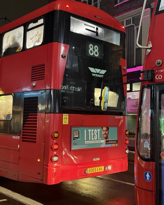 Back of a red bus. There is an advert on the bus that reads 'I Test'.