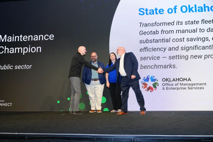 Geotab founder and CEO Neil Cawse shakes hands with OMES Fleet Systems Manager Jed Redeker in front of OMES Fleet Director Nathan Pumphrey and OMES Fleet Service Advisor Brandi Evans at the 2026 Geotab Connect ceremony.