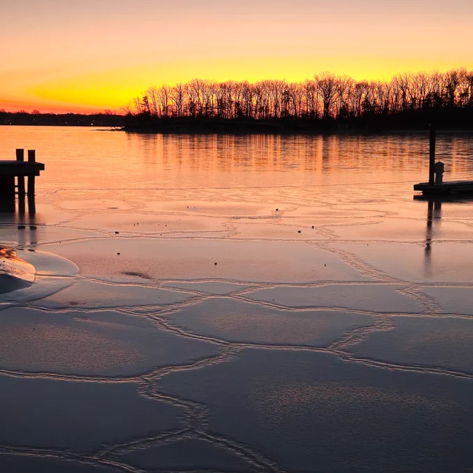 Two docks jut out into ice-covered water under a sunrise that colors the ice pink and purple.