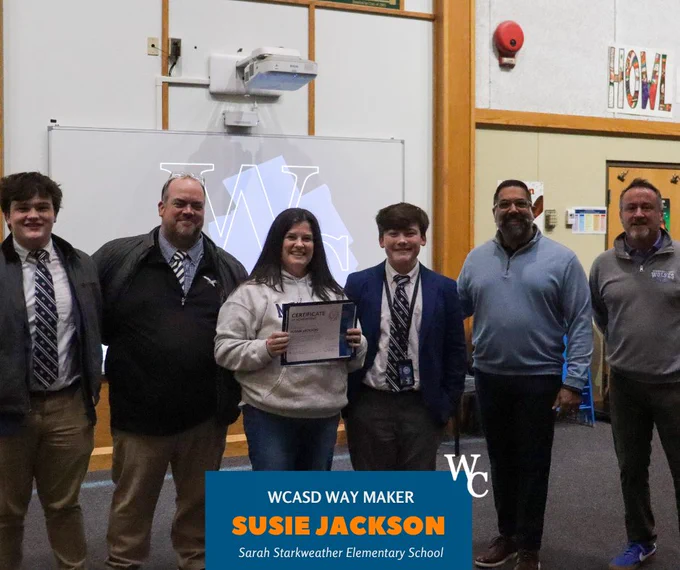 Susie Jackson from Sarah Starkweather Elementary holds a certificate as WCASD Way Maker, standing with five men in a school setting.