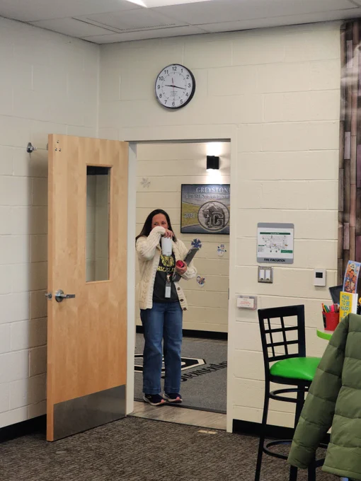 Woman standing in a doorway in a classroom or office setting.