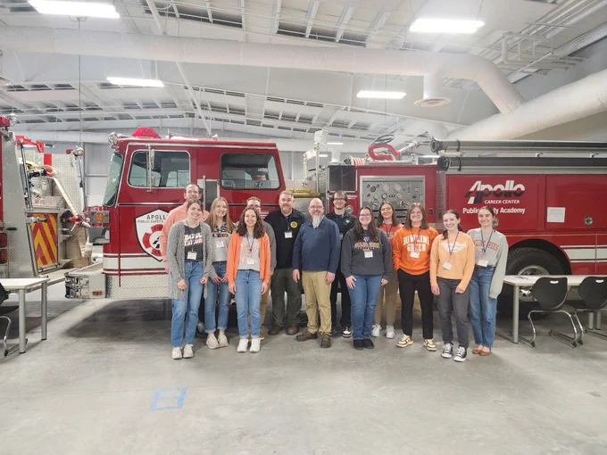 Students and faculty standing in front of a red firetruck wearing BGSU sweatshirts and name tags.