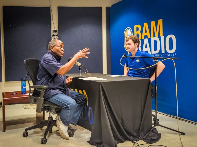 Two individuals sitting in a podcast studio doing a podcast. 