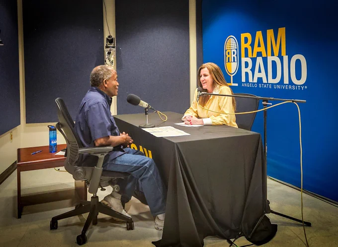 Two individuals sitting in a podcast studio doing a podcast. 