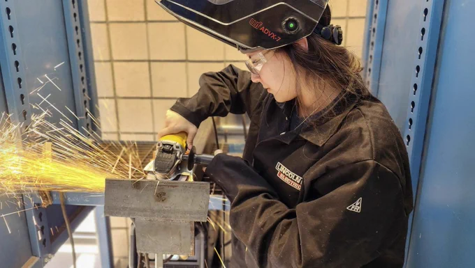 Female welding student using a grinder with sparks visible