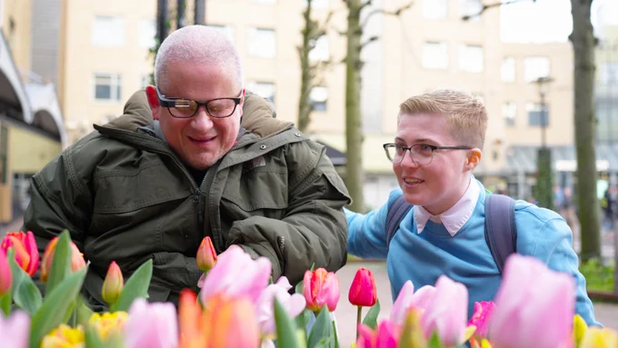 A photo of Brian Dalton, a long time blind Envision user, with his assistant Rachel in front of a bunch of tulips and Brian is using the Envision Glasses to get a vivid description of what's in front of him.