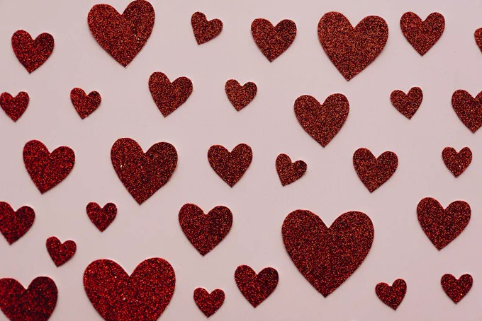 Sparkling red glitter hearts scattered on a light surface, perfect for Valentine's themes.