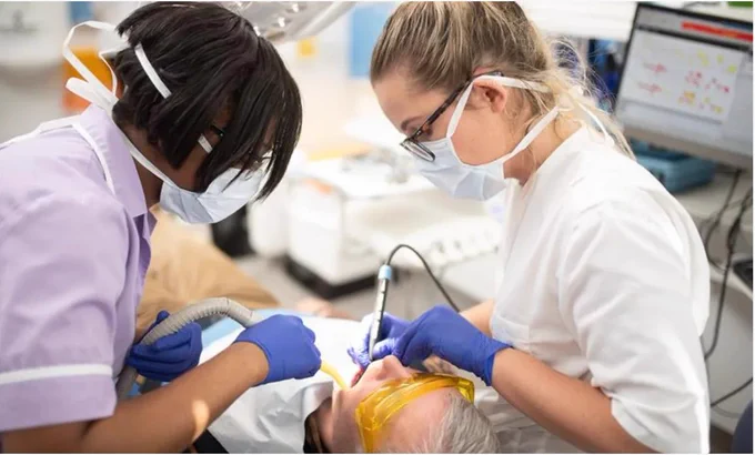 Two female dental practitioners treat a male patient.