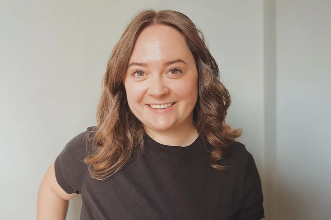 Erin Schuler has brown hair that she is wearing loosely curled and parted down the middle. She's wearing a dark brown shirt and smiling at the camera.