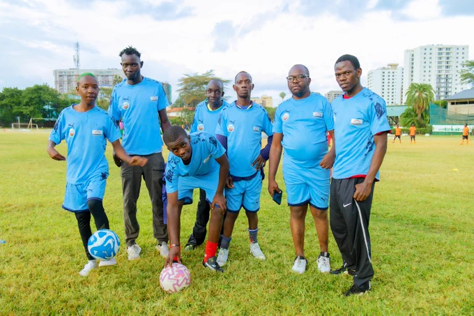 A group of 8 players wearing matching football uniforms on a grassy field posing confidently during an inclusive football tournament.