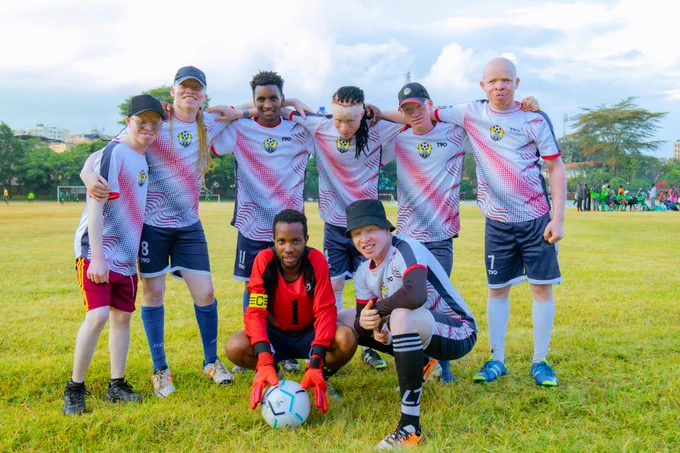 A group of 8 players wearing matching football uniforms on a grassy field posing confidently during an inclusive football tournament.