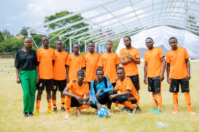 A group of 12 players wearing matching football uniforms on a grassy field posing confidently during an inclusive football tournament.